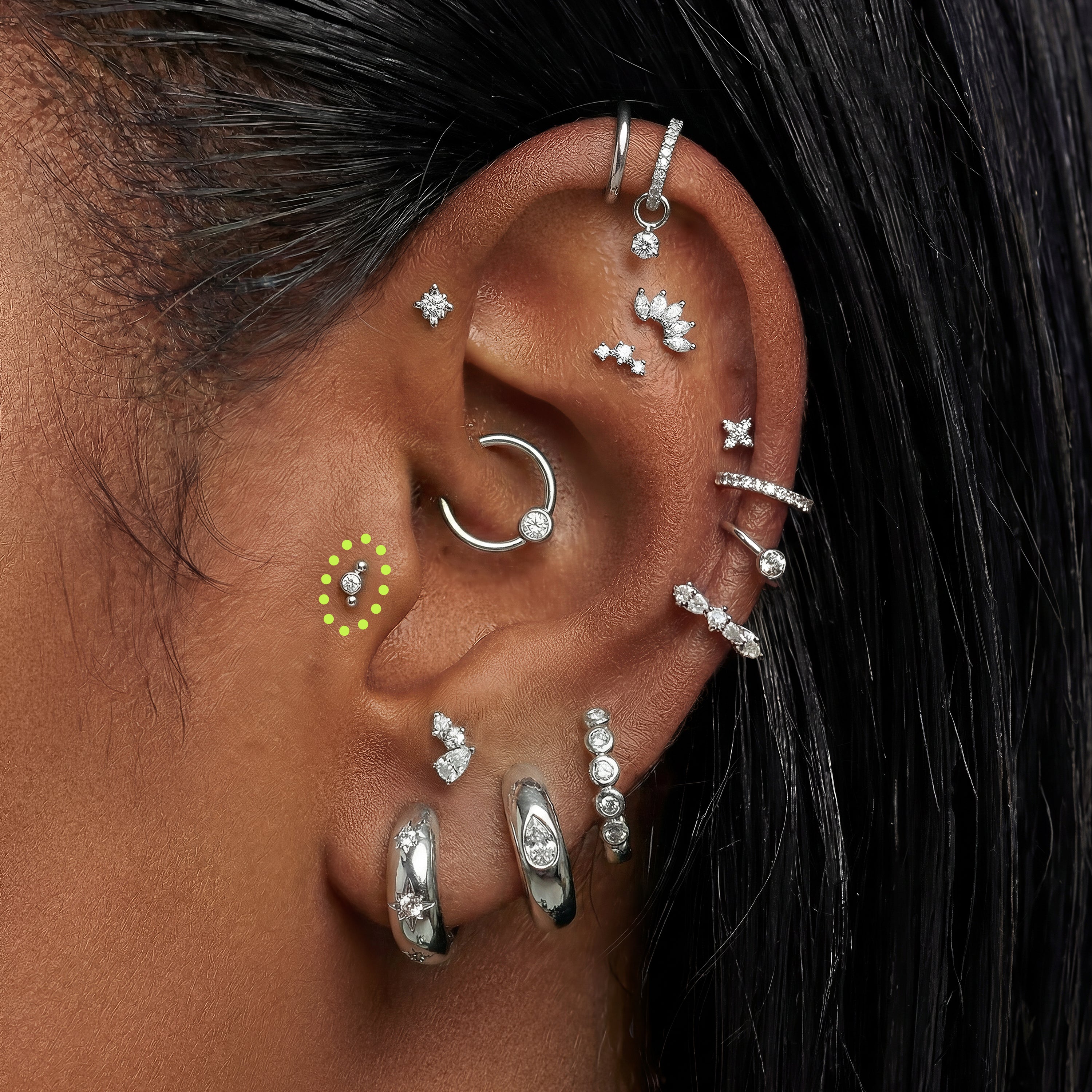 Close-up of an ear with multiple silver earrings stone earrings and a micro bezel cluster flatback circled in the tragus