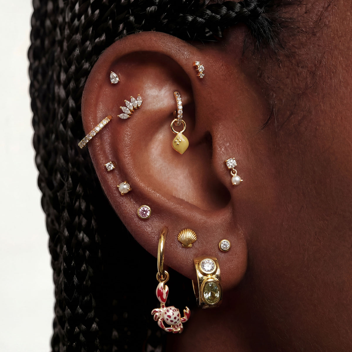 This image shows an ear with a 14k gold plated huggie with a crab charm and a huggie with an lemon charm 