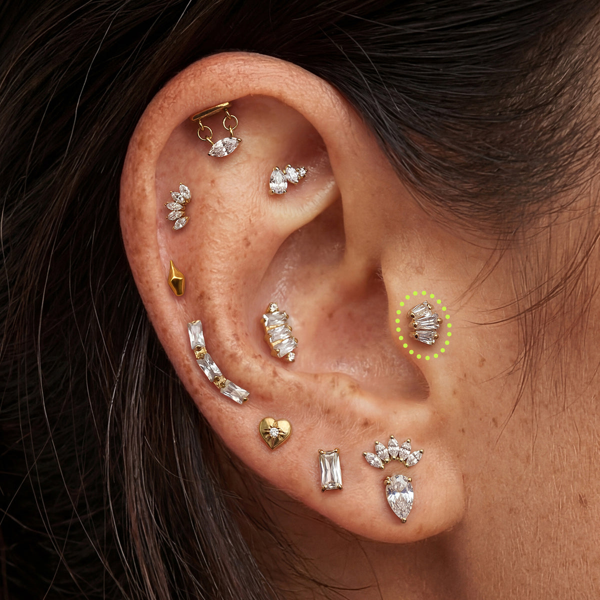 This is an image of a gold toned flatback stud that has three clear baguette cut CZs forming a crown shape circled on an ear.