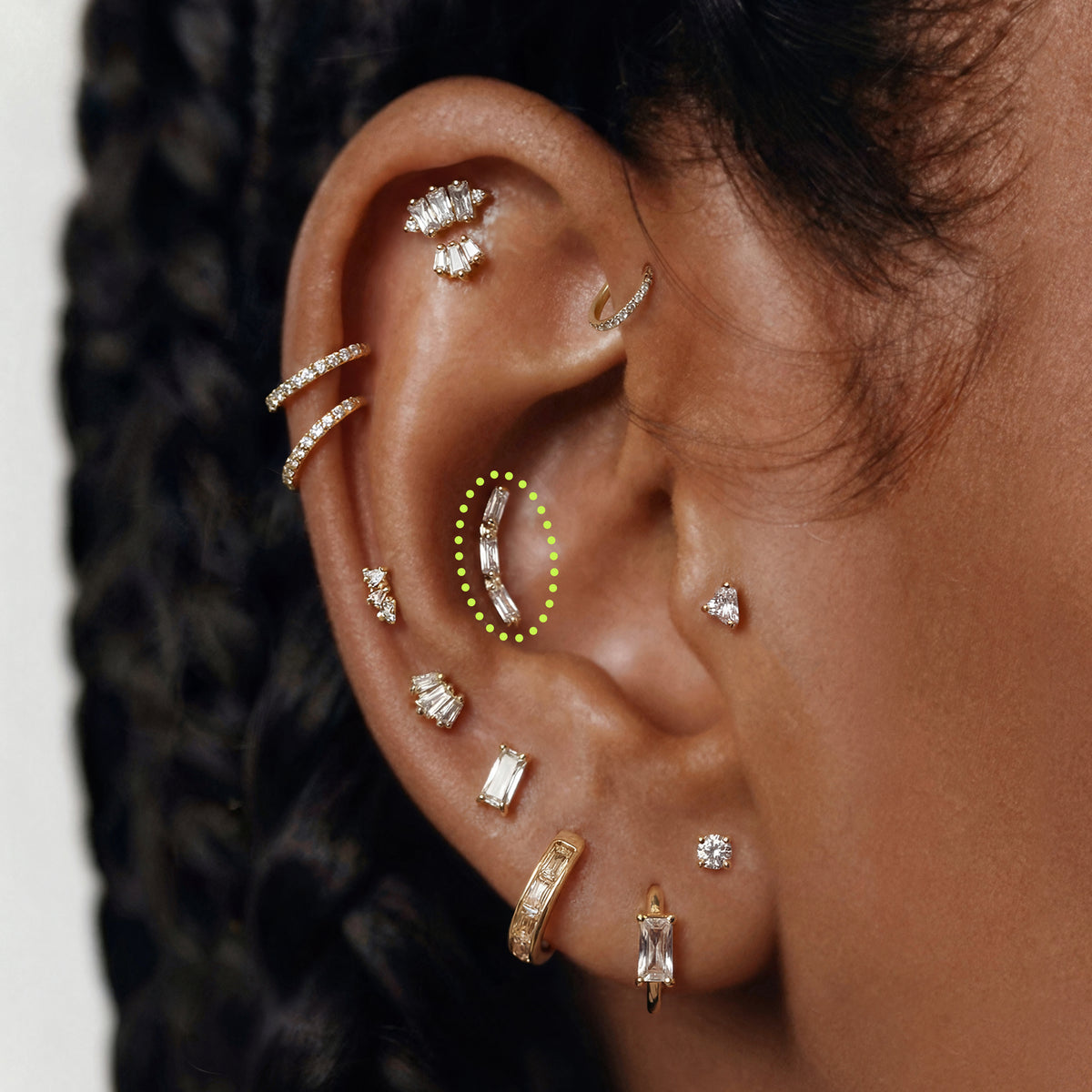 This is an image of a gold toned flatback stud that is in the shape of a curved bar and consists of three baguette cut, clear CZ stones circled on an ear.