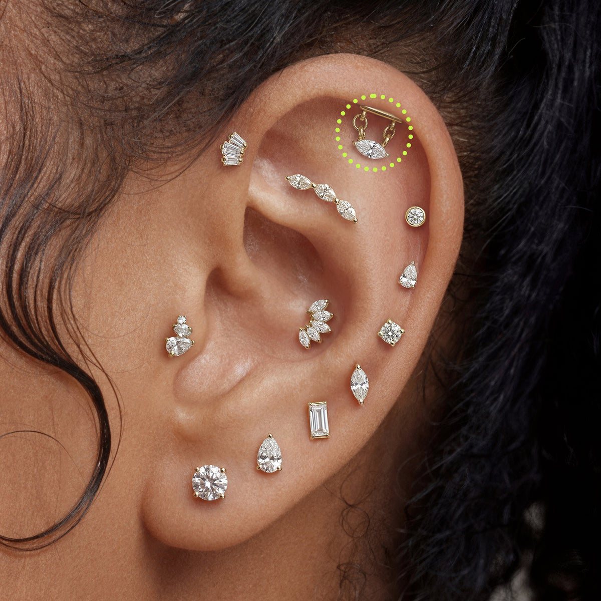 This is an image of a gold toned flatback stud that has a gold bar with chains hanging from both sides supporting a clear, marquise cut CZ stone circled on an ear.