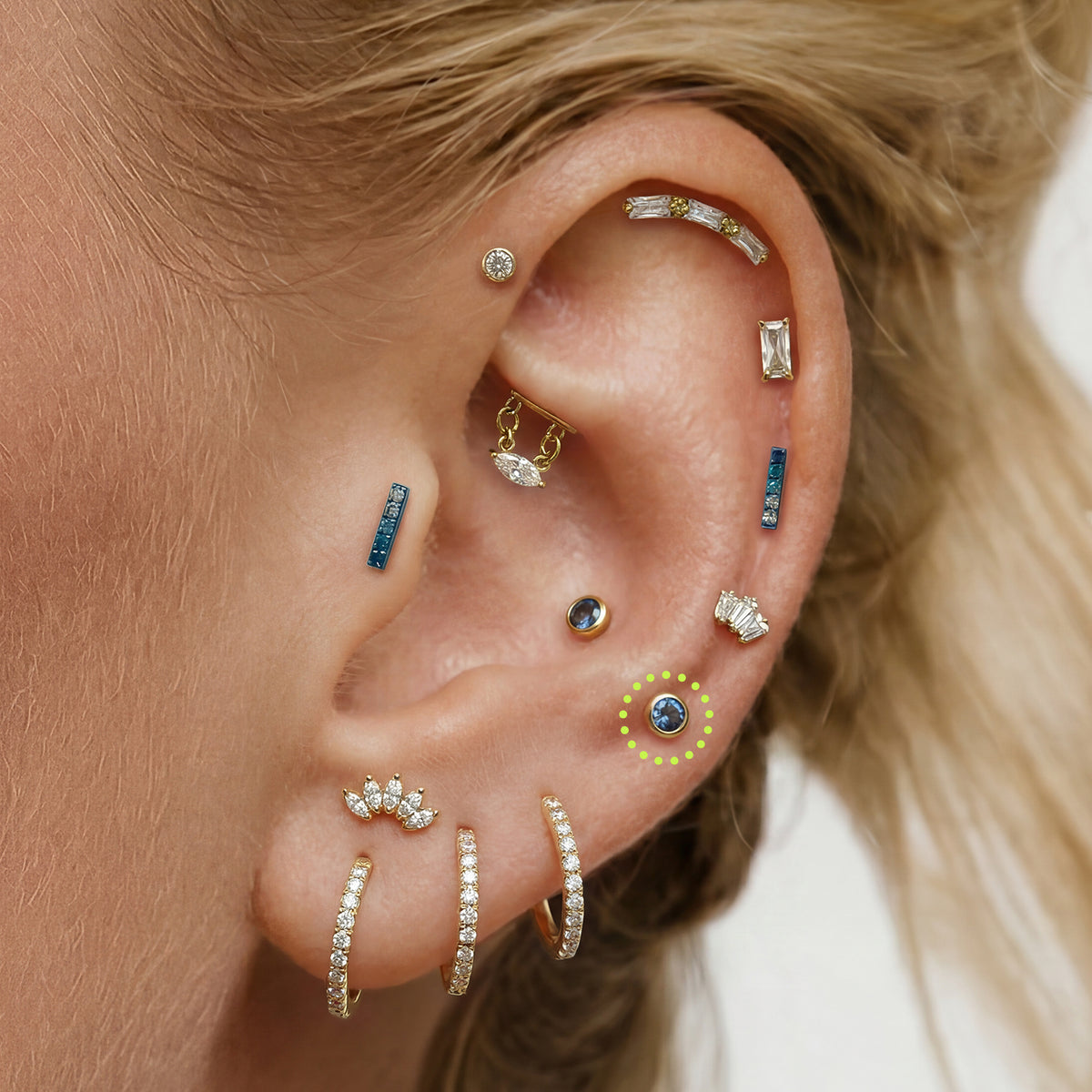 This is an image of a gold toned flatback stud with a 3mm, bezel set blue CZ stone circled on an ear.