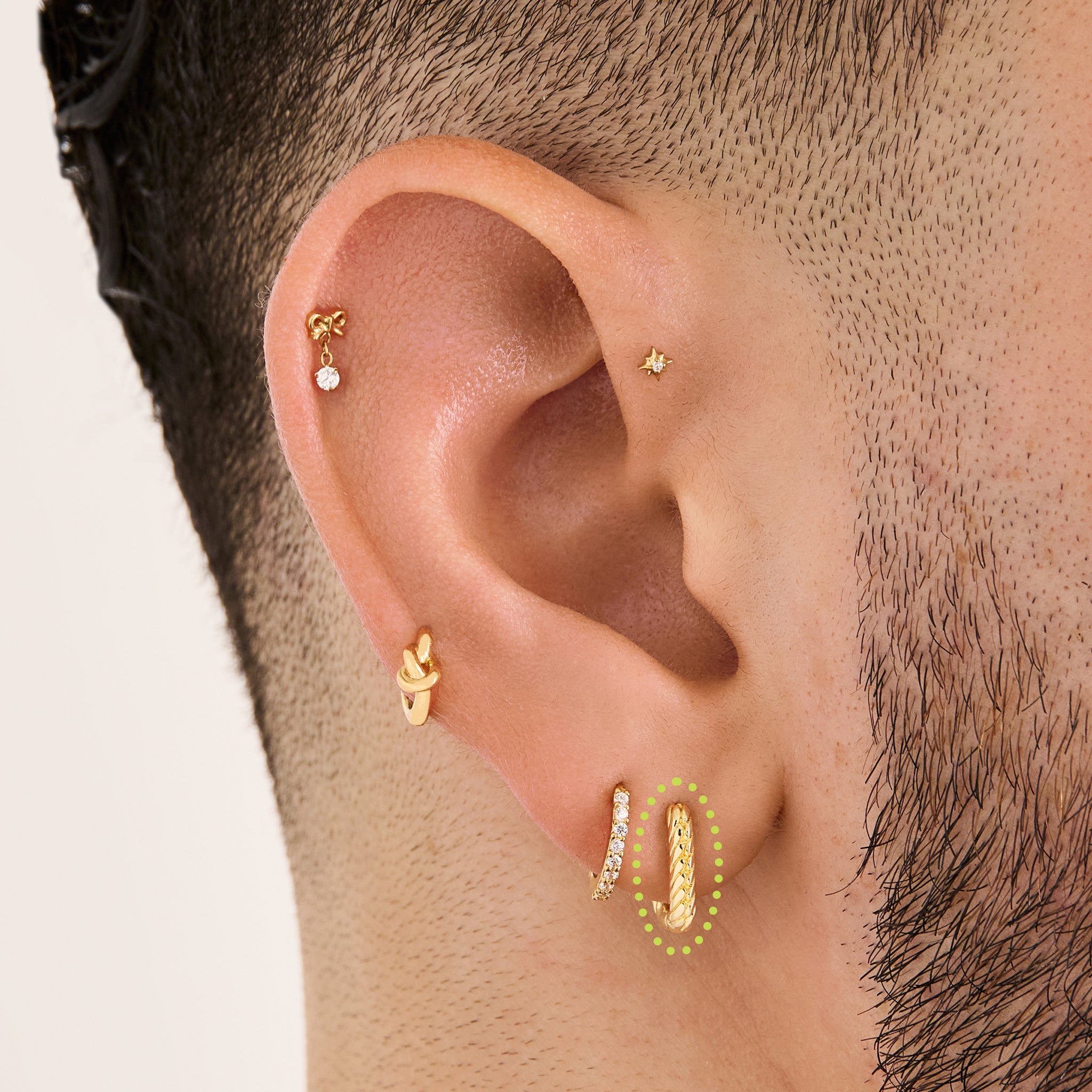 This is an image of a gold-toned, square shaped huggie that has twists throughout it on ear. [hover] color:null|gold