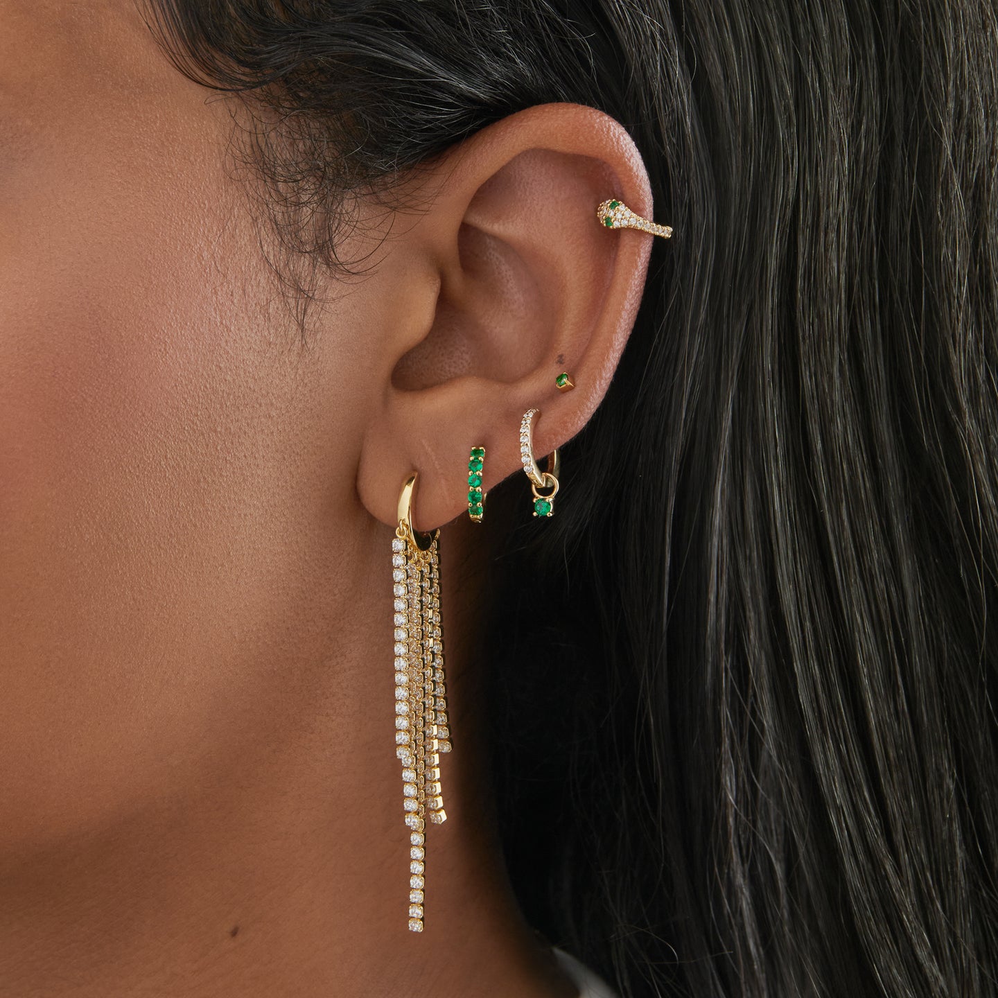 This is an image of a gold huggie that has gold/clear CZ strands dangling from it in a fringed pattern on ear. [hover] color:null|gold/clear