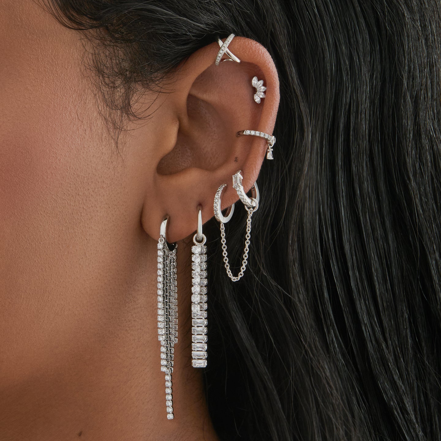 This is an image of a silver huggie that has silver/clear CZ strands dangling from it in a fringed pattern on ear. [hover] color:null|silver/clear