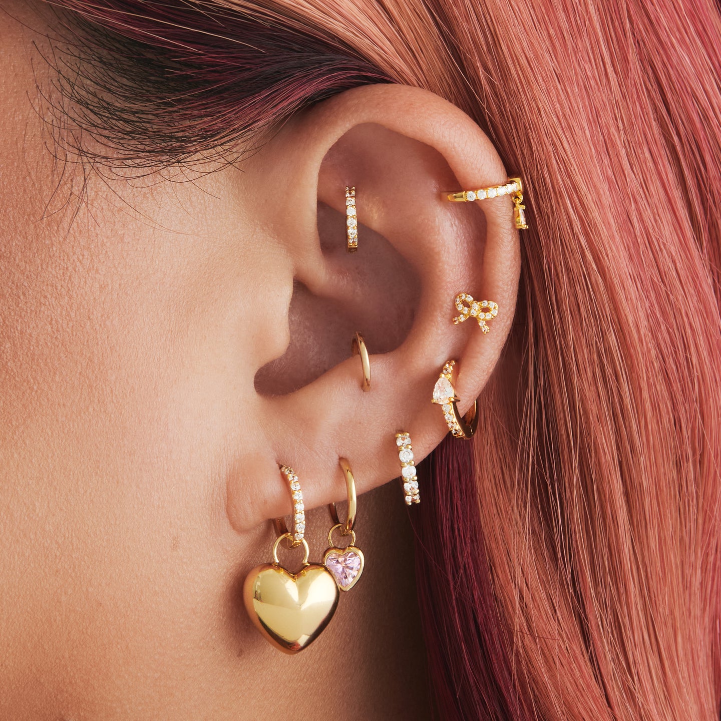 An image of a gold/clear mini pave huggie with a gold, puffy heart shaped charm on ear. [hover] color:null|gold/clear