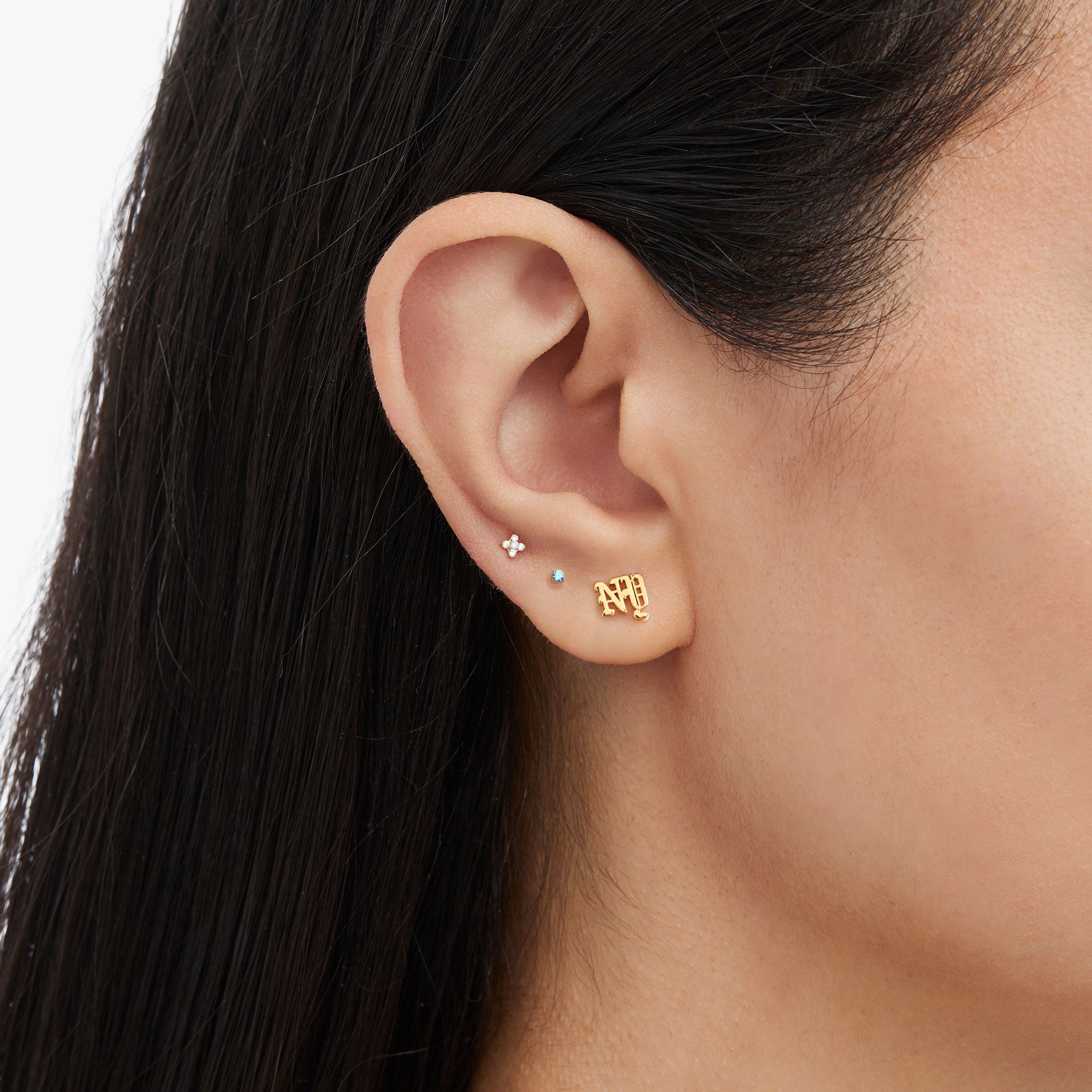 On ear image of a gold earscape Set for the NY Knicks featuring a NY flatback stud, a micro blue cz flatback stud, and a pave x flatback stud 