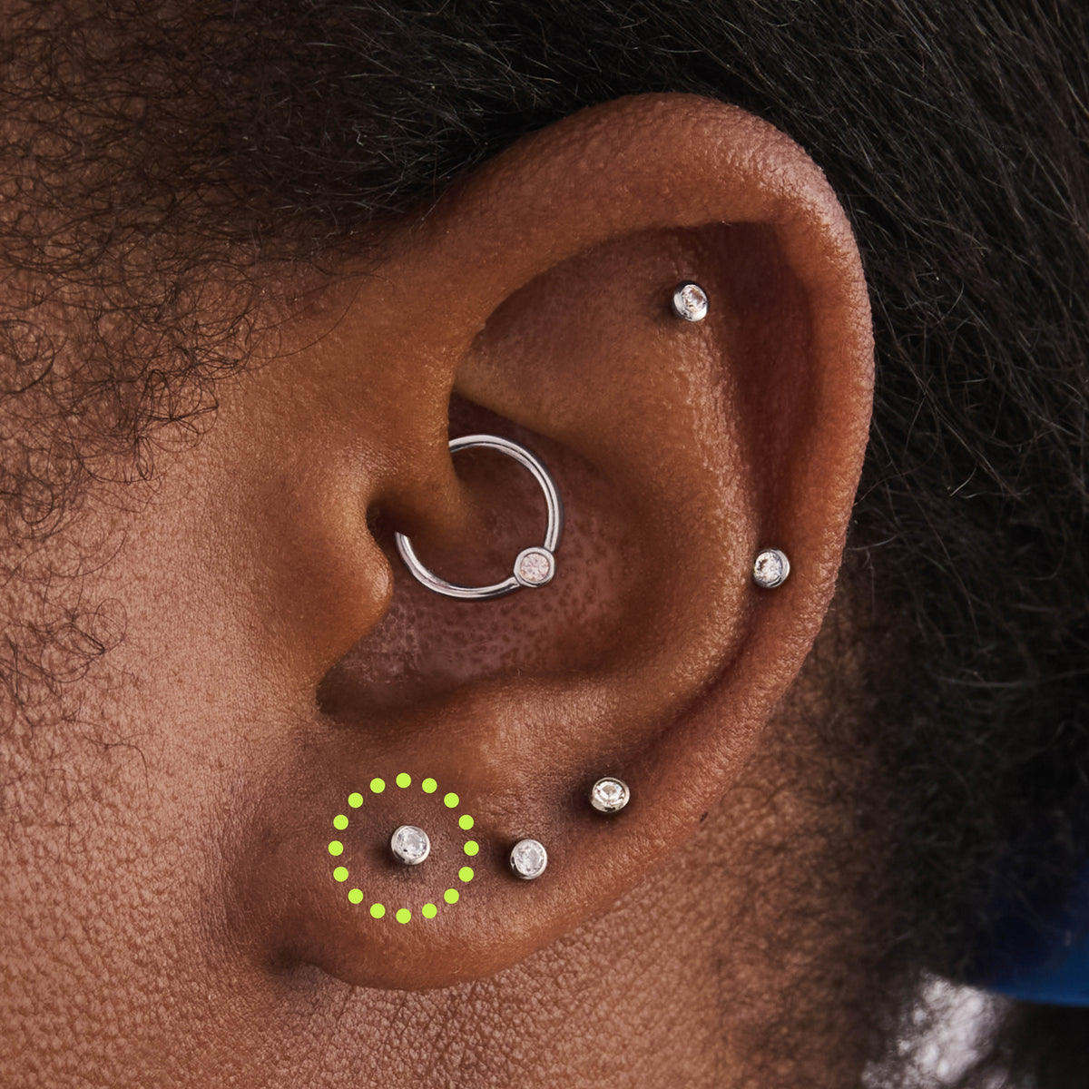 This image is a silver toned titanium flatback stud with a bezel setting and clear CZ stone circled on an ear.