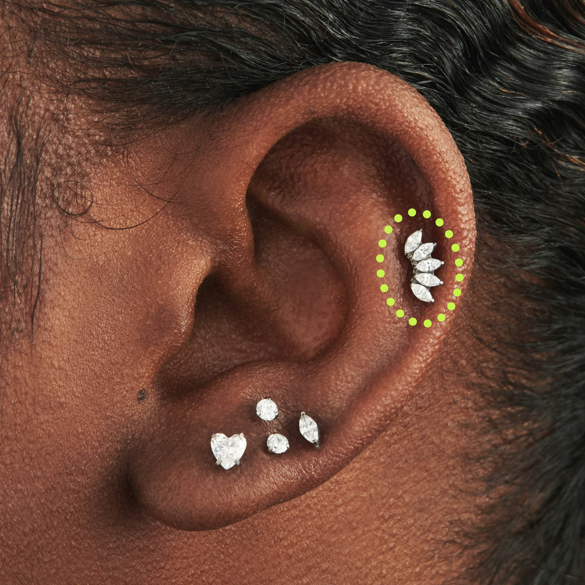 This image is a silver toned titanium flatback stud that features 5 marquise set crystal CZs in a crown shape circled on an ear. - Alternative view 1