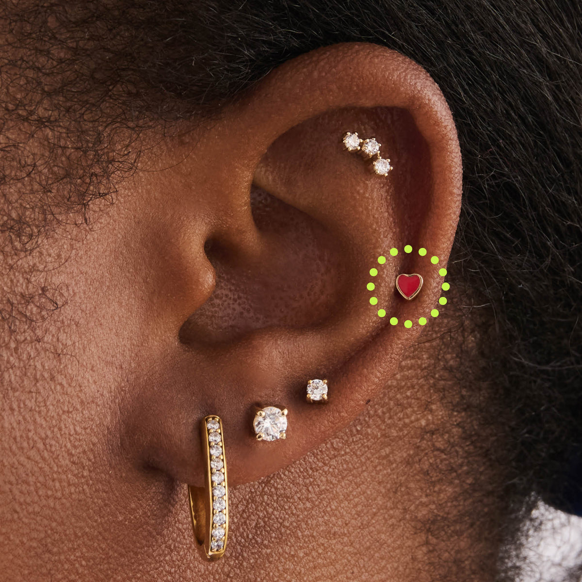 This image is a heart-shaped 14K gold flatback stud with a red enamel filling circled on an ear.