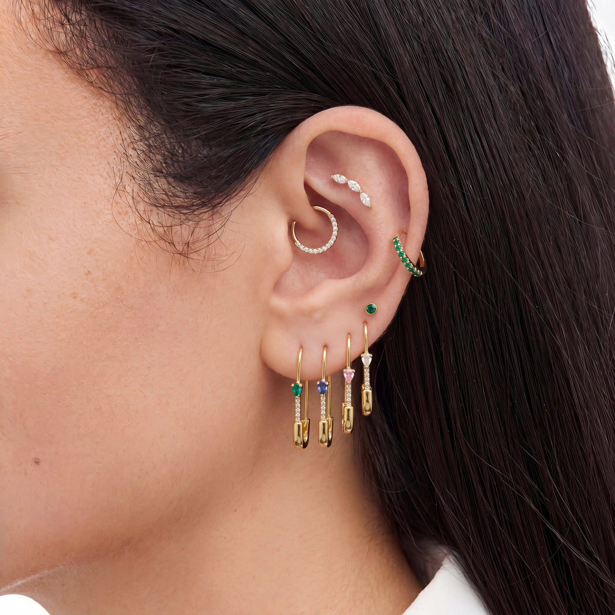 This is an image of an ear displaying the pave pear safety pin earring in 4 different colors on ear--In gold/green, gold/blue, gold/pink, and gold/clear color ways.