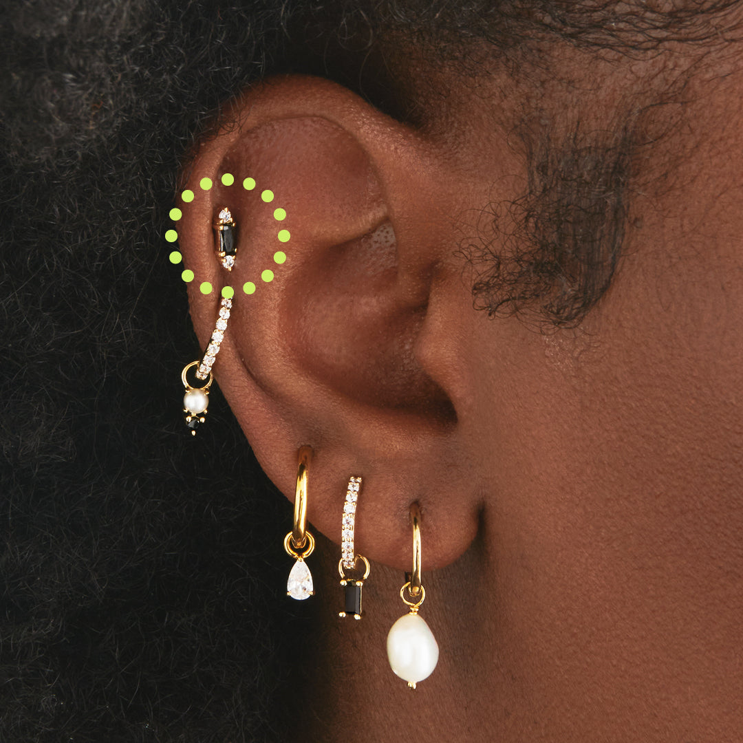 A black baguette-shaped CZ stud with two gold/clear CZs on the end of the baguette on ear. [hover] color:null|gold/black