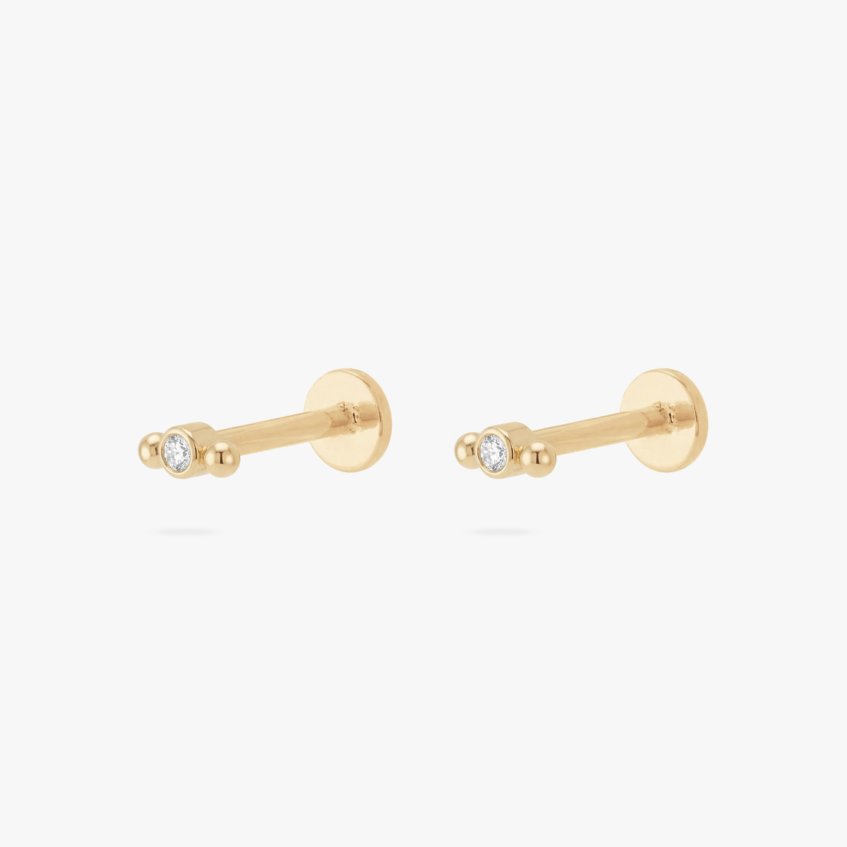 Pair of gold fkatback earrings with small bezel stones and balls on a white background