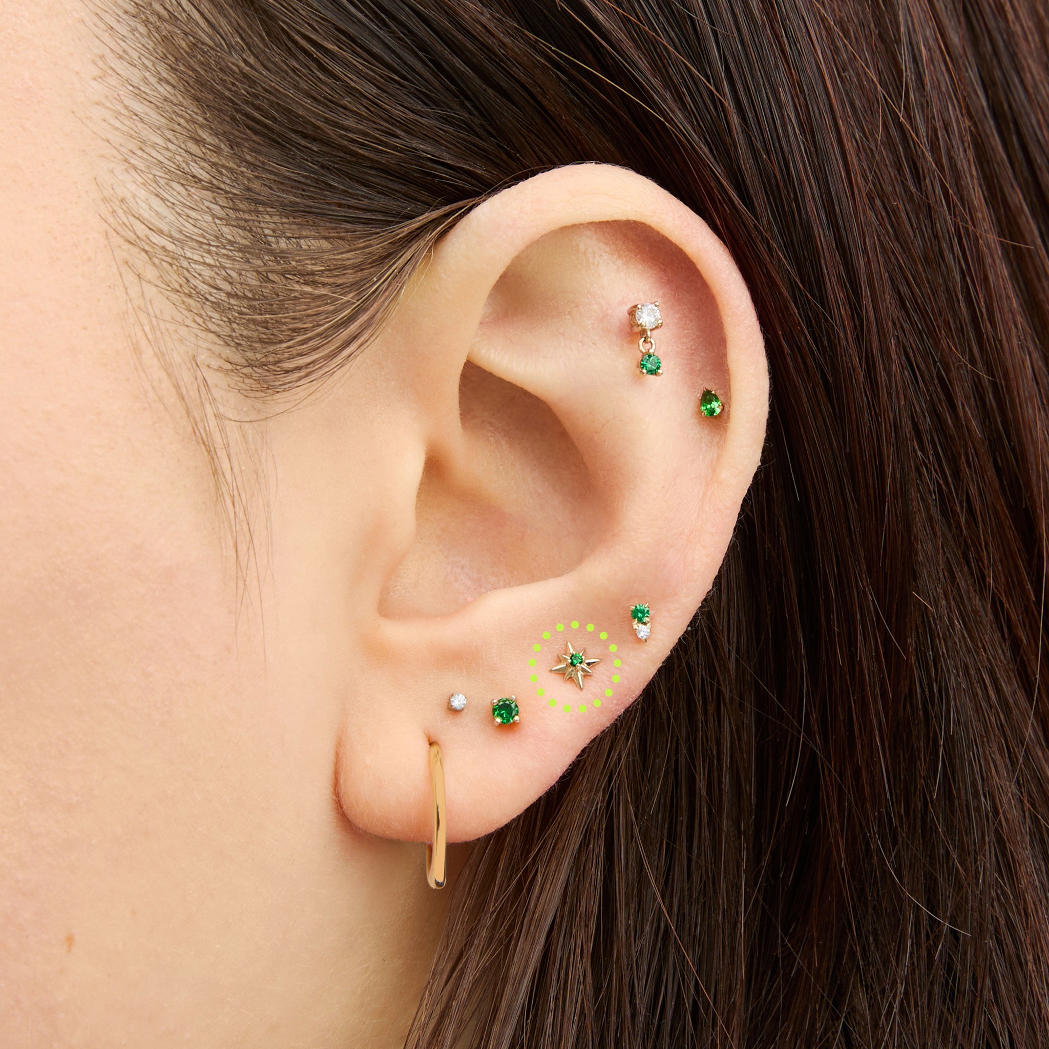 This is an image of a 14K gold flatback stud with a pointed star with a green cz stone in the center on ear. [hover] color:null|gold/green