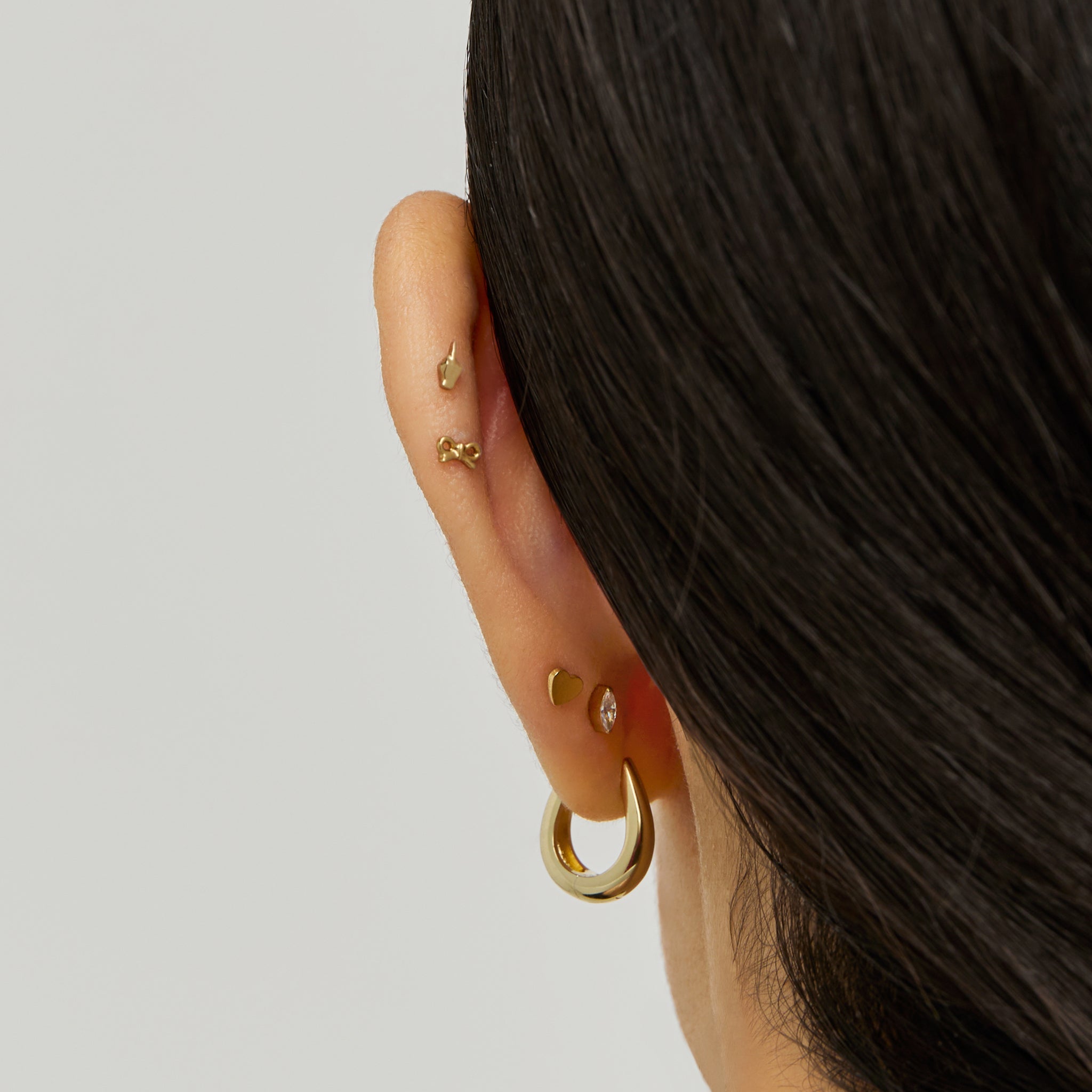 This is an image of a gold-toned flatback stud that is in the shape of a middle finger on ear. color:null|gold