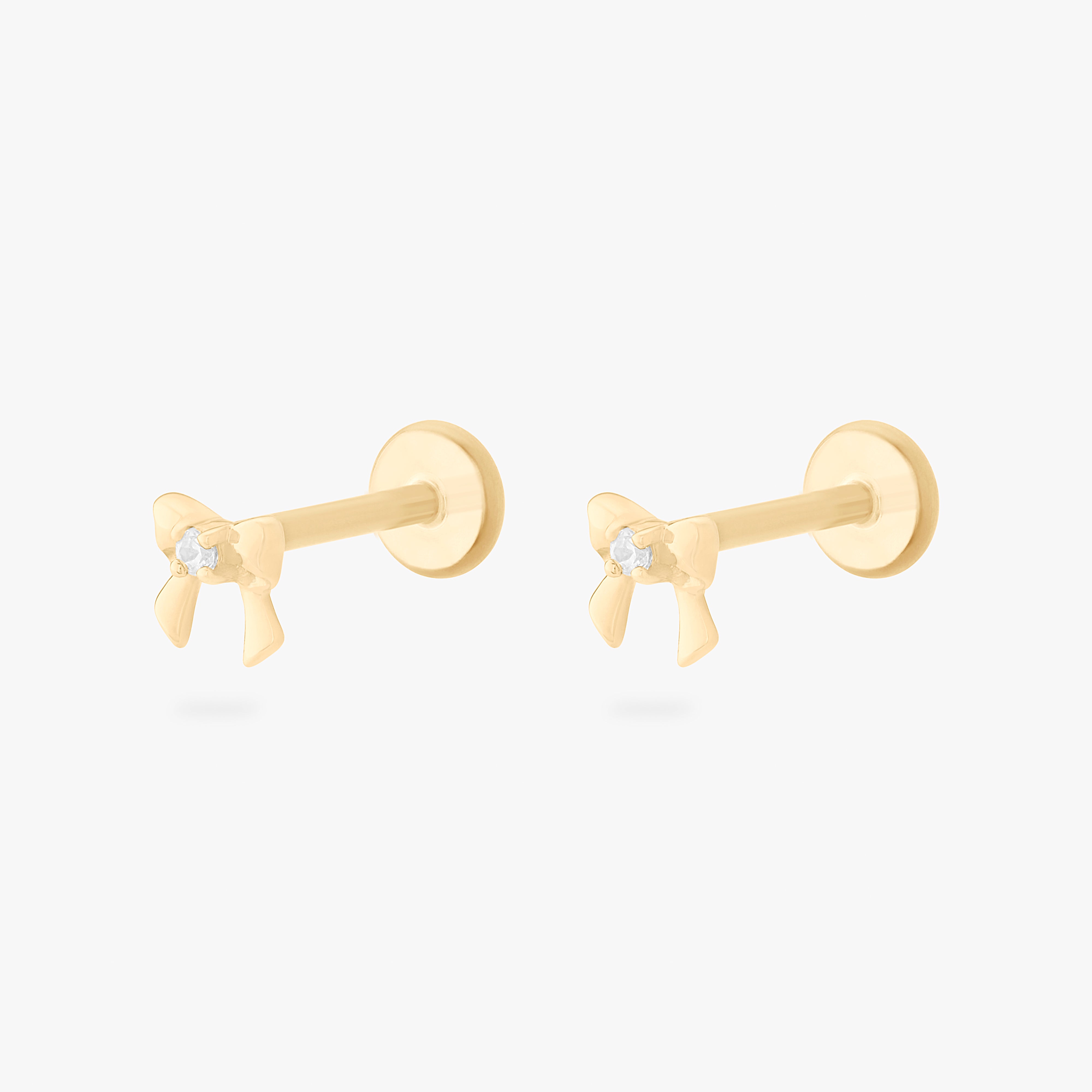 This is a pair of 14k gold flatback studs that are bow shaped with a clear cz in the middle of both. [pair] color:null|14k gold/clear
