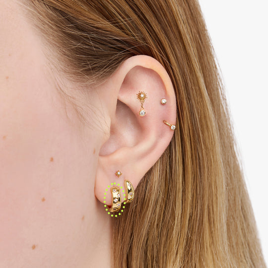This image displays a 14K gold plated chunky huggie that features twinkle star shaped engravings with crystal CZ stones throughout the huggie circled on an ear.