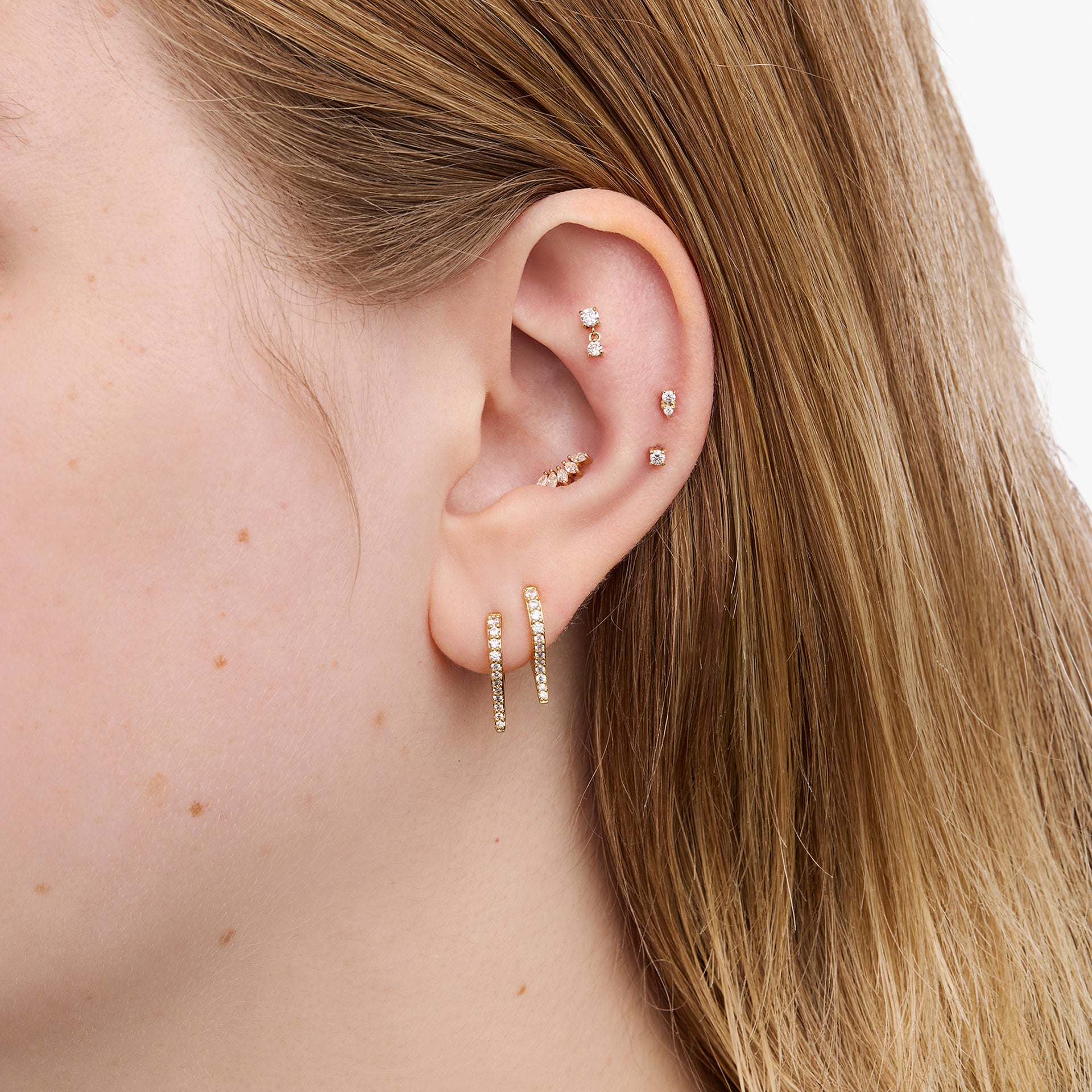 Close-up of an ear with multiple gold earrings against a neutral background