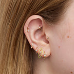 Gold hoop earring with embedded stones on a white background on an ear.
