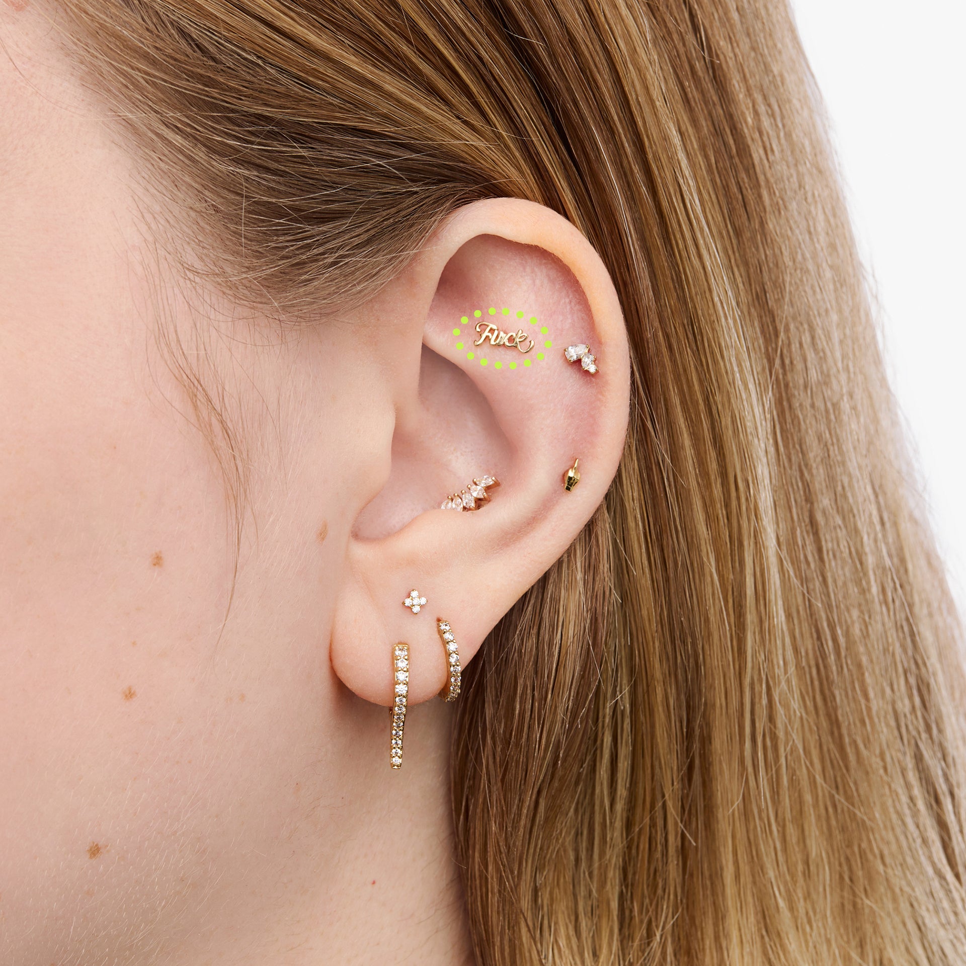 Close-up of an ear with multiple gold earrings on a neutral background