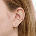 Close up of gold cat shaped earrings on an ear on a neutral background