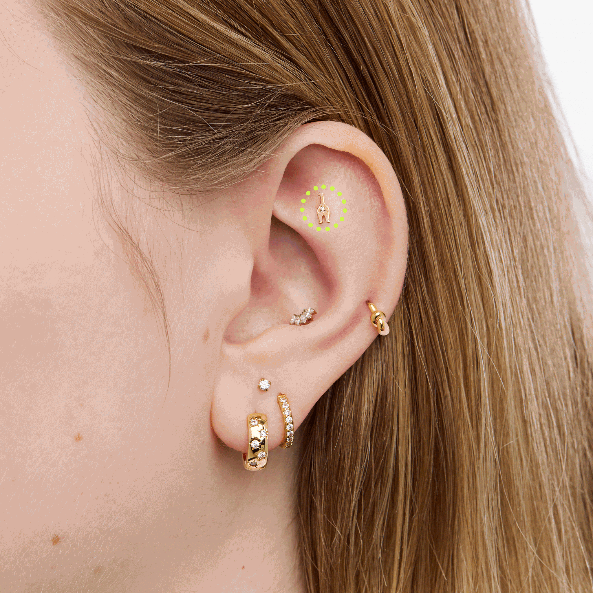 Close up of gold cat shaped earrings on an ear on a neutral background