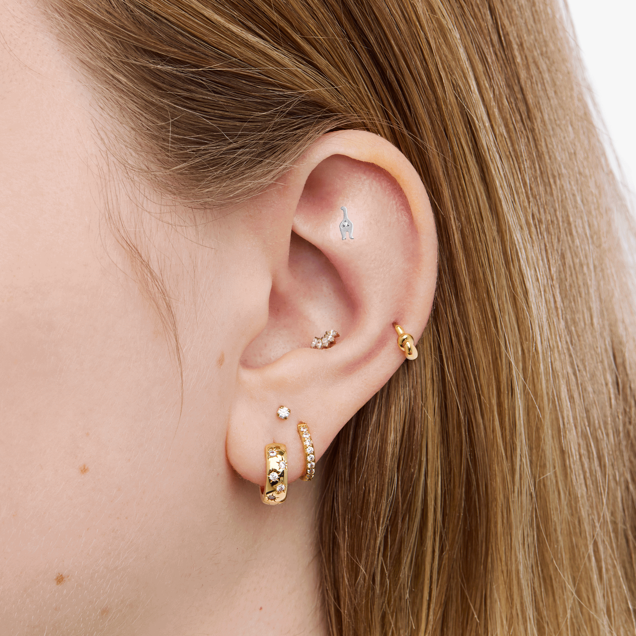This is an image of a silver toned titanium flatback stud that is shaped like a cat. This flatback top has a kitten face, and the flatback post has the kitten body. This image is a rotating GIF displaying both sides of the flatback studs on an ear. 
