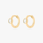 Gold huggie earrings with clear gemstones on a white background