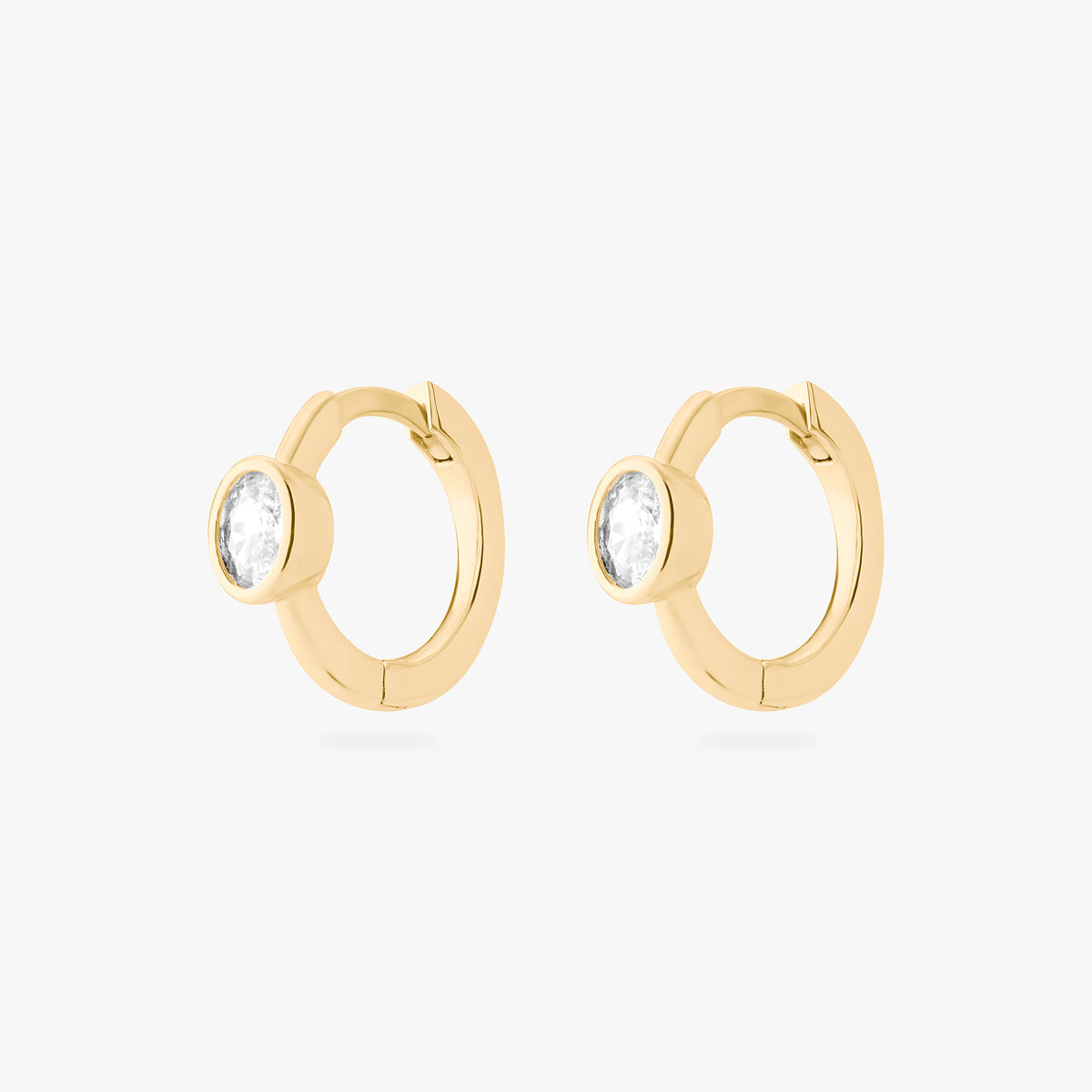 Gold huggie earrings with clear gemstones on a white background