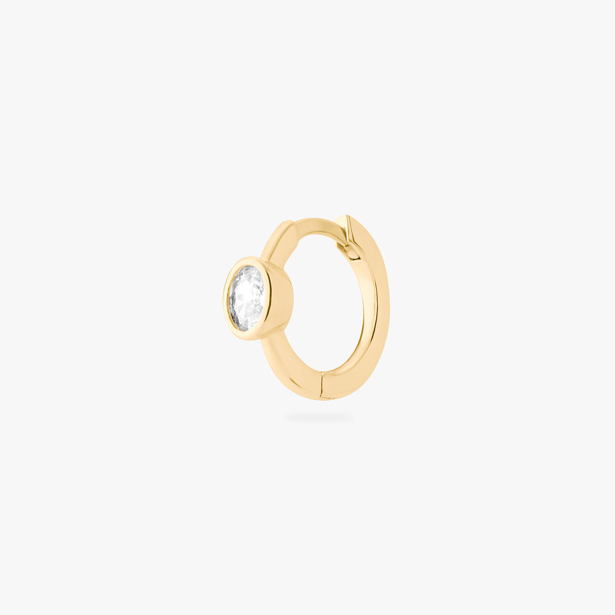 Gold huggie earring with a clear gemstone on a white background