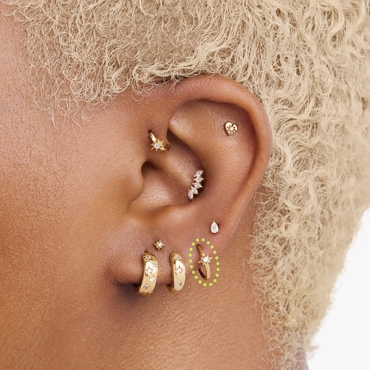 A single gold earring with a star-shaped stone, shown circled on an ear.