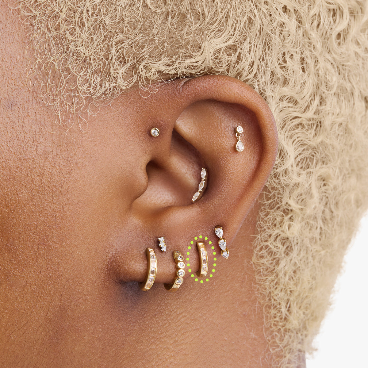 This is an image of a 14K gold plated huggie earring with 4 baguette cut, bezel set crystal CZs along the edge circled on an ear.