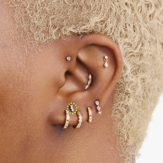 This is an image of a gold-toned titanium flatback stud with 3 micro baguette cut stones placed in a cluster circled on an ear.