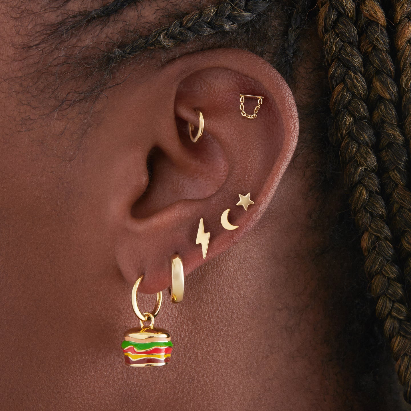 This is an image of a burger-shaped, enameled charm huggie in gold created to look like a Shake Shack Burger on ear. [hover] color:null|gold/clear