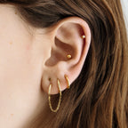Two separate hoop earrings connected by a chain. [hover] color:null|gold