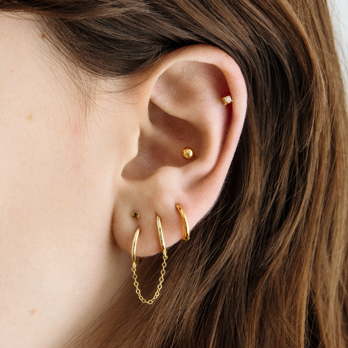 Two separate hoop earrings connected by a chain. [hover] color:null|gold