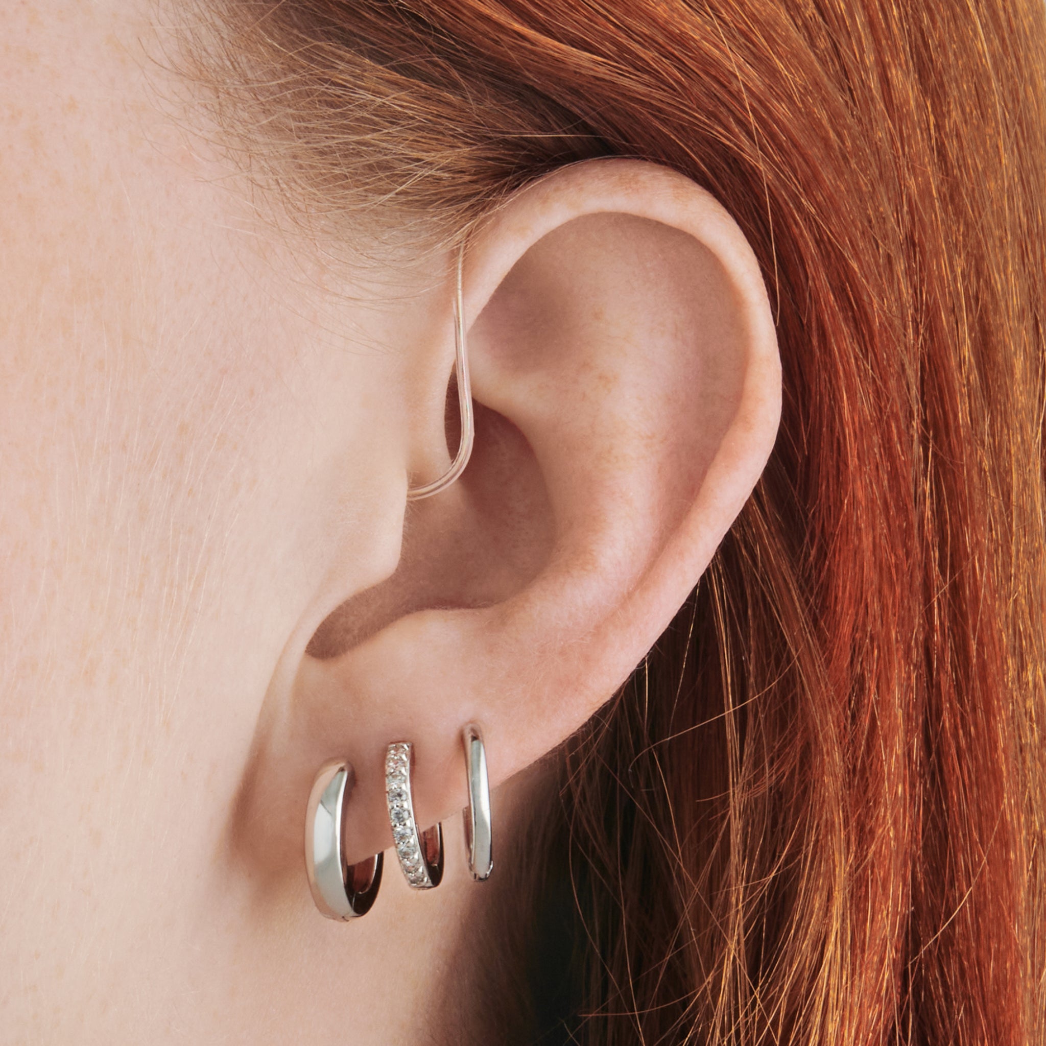 a set consisting of a pair of silver mini chunky huggies, silver mini pave huggies, and silver small slim huggies on ear [hover] color:null|silver