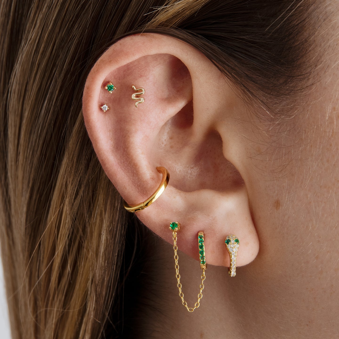 This is a gold, pave lined and serpent shaped huggie earring with green CZ eyes [hover] color:null|gold/clear