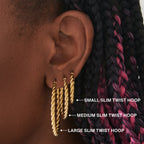 a large gold slim twisted hoop earring on ear 
