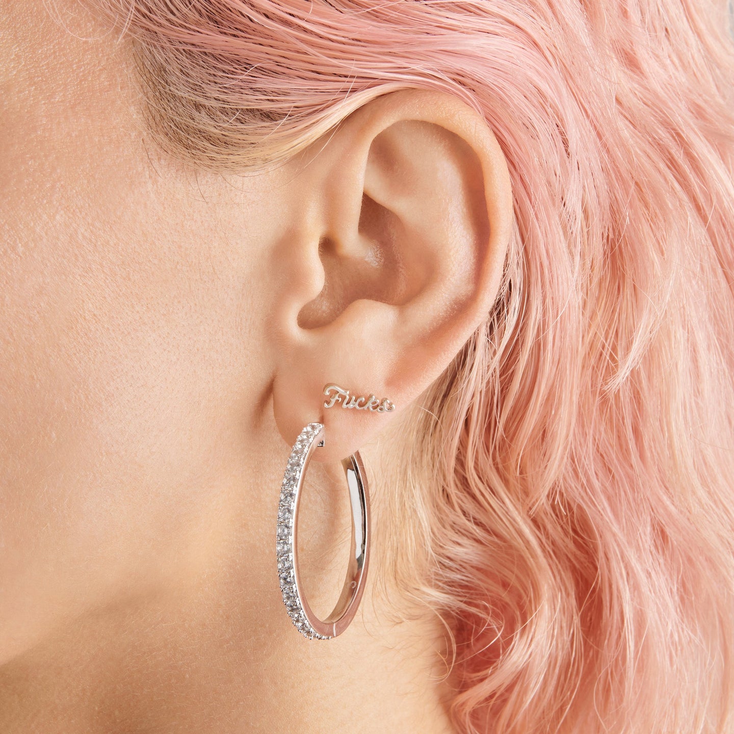 a silver stud that spells out fucks in cursive writing on ear [hover] color:null|silver