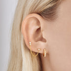 This is a small gold huggie that has small pearls lining the front of it on ear color:null|gold