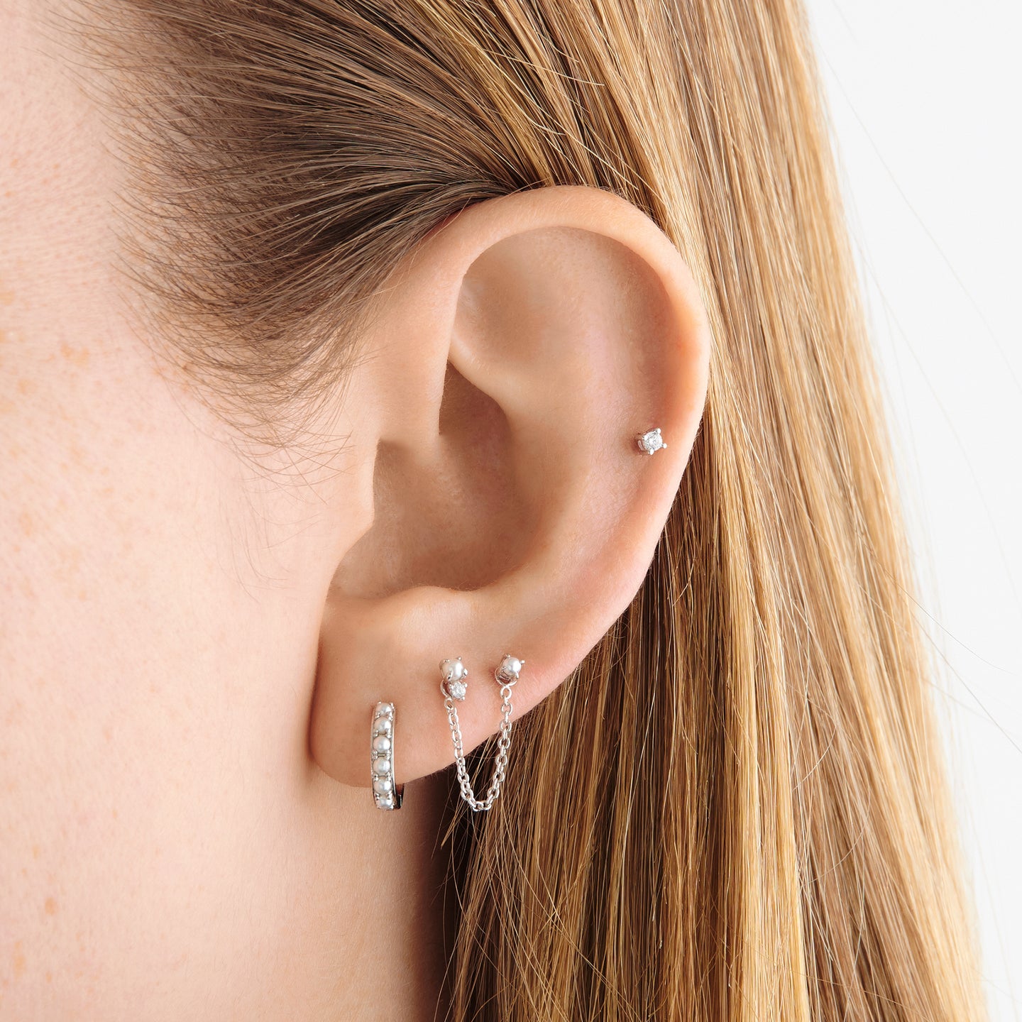 This is a small silver huggie that has small pearls lining the front of it on ear [hover] color:null|silver