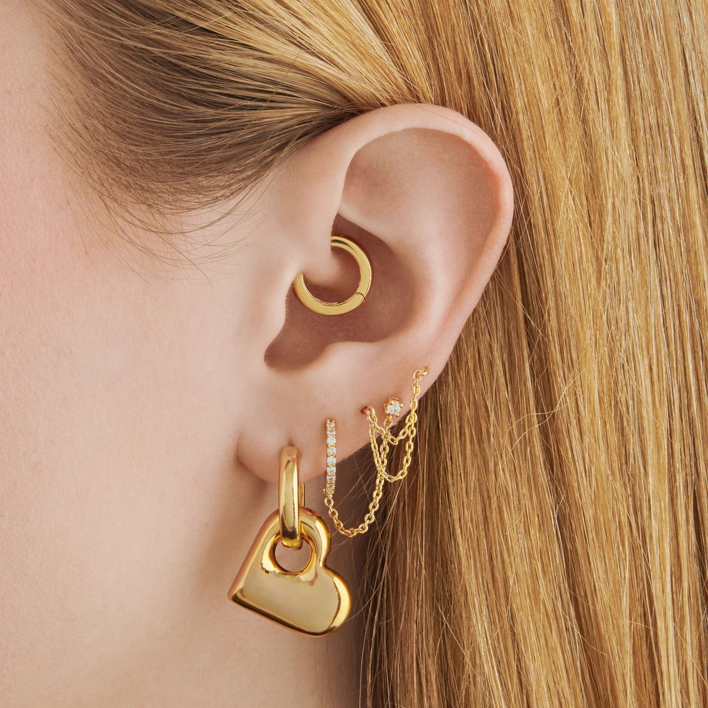 a chunky gold hoop that has a gold puffy heart charm on it on ear [hover] color:null|gold