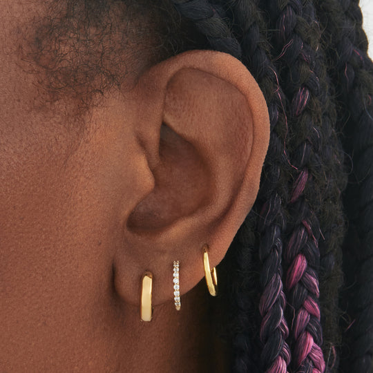 a set consisting of a pair of gold mini chunky huggies, gold mini pave huggies, and gold small slim huggies on ear [hover] color:null|gold