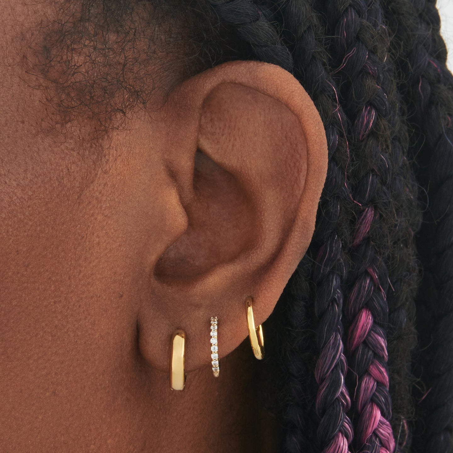 a set consisting of a pair of gold mini chunky huggies, gold mini pave huggies, and gold small slim huggies on ear [hover] color:null|gold