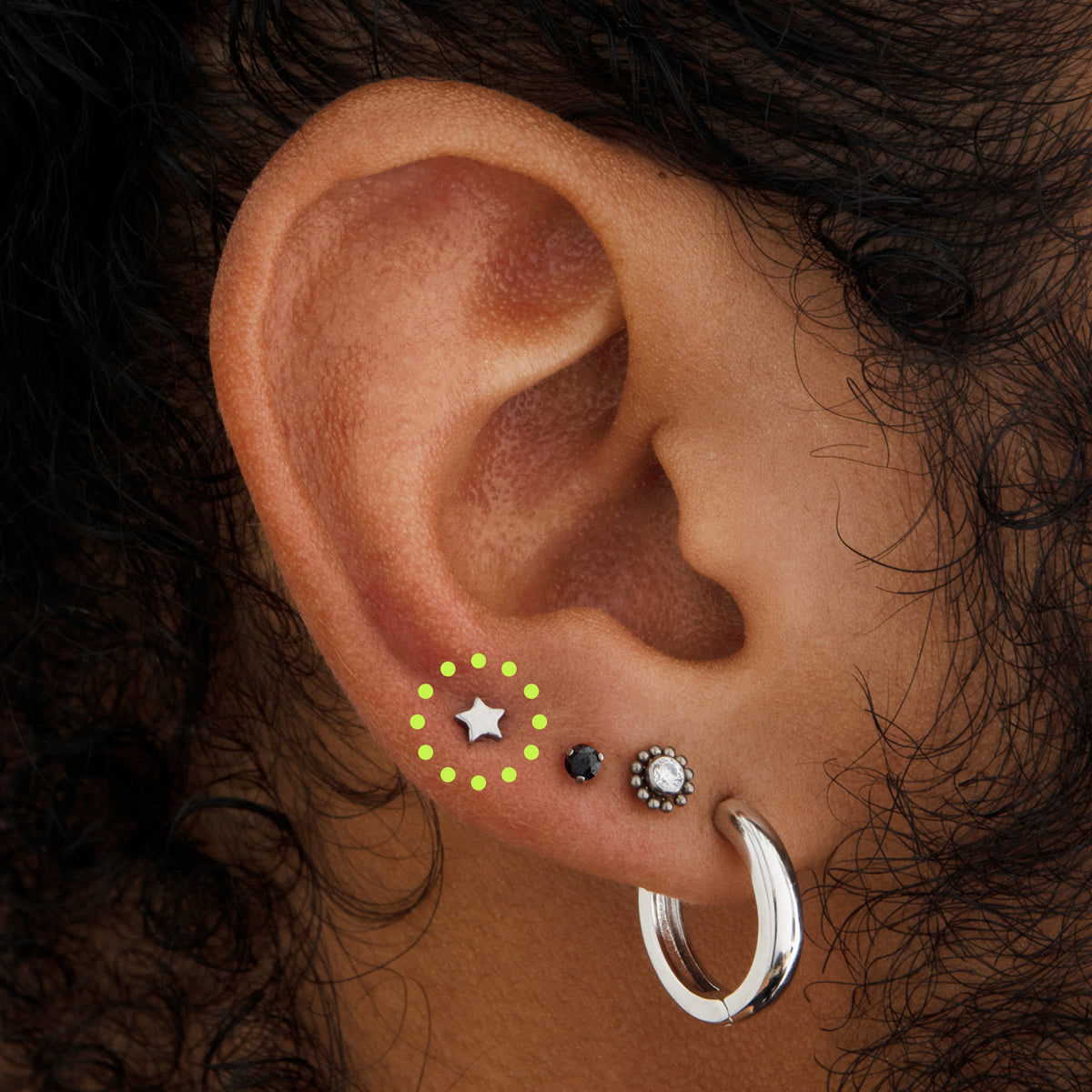 This image is a silver toned titanium star-shaped flatback stud circled on an ear.